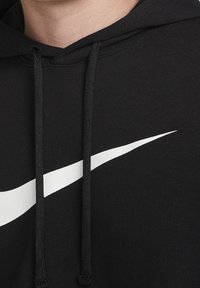 Nahaufnahme eines schwarzen Hoodies mit weißem Nike-Swoosh-Logo und schwarzen Kordeln im Halsbereich.