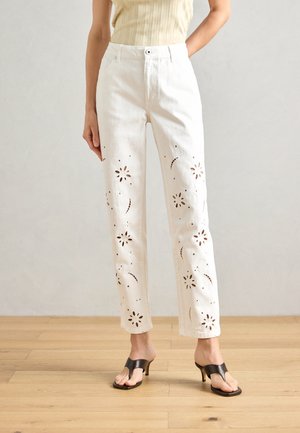 I pantaloni in denim bianco presentano dei motivi floreali ritagliati lungo le gambe, con una vestibilità dritta e un classico design a cinque tasche. Abbinati a sandali neri con tacco.