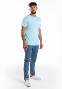 Hellblaues Baumwoll-T-Shirt mit kurzen Ärmeln und rundem Halsausschnitt, kombiniert mit hellblauen Jeans und weißen Sneakers.