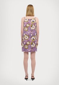 Robe à motif floral violet avec des bretelles spaghetti, présentant des motifs de fleurs blanches et vertes sur un fond texturé.