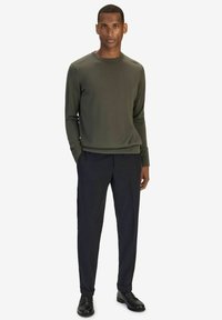 Mörkgrön ribbad långärmad tröja i kombination med mörka byxor och svarta skor. Enkelt runt halsringning, figurnära passform och minimal detaljering.