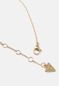 Colar de corrente em ouro com fecho tipo lagosta, apresentando elos circulares e um pendente triangular gravado com a palavra "GUESS."