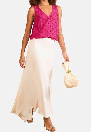 Fuchsia mouwloze top met textuur van ronde bulten, gecombineerd met een vloeiende witte maxi rok. Model houdt een beige tas met een gouden accent vast.