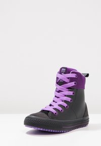 Czarny sneakers wysokiej góry z fioletową cholewką zamszową, wyposażony w jasnofioletowe sznurowadła, teksturowaną gumową podeszwę oraz wzmocniony nosek.