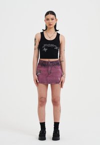 Zwarte cropped tanktop met zilveren grafisch ontwerp; roze denim minirok met bloemborduursel; model draagt zwarte platformschoenen met sokken.