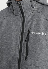 Veste zippée grise en tissu texturé, dotée d'une capuche, d'une fermeture éclair contrastante et d'un petit logo Columbia sur la poitrine.