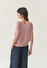 Lichtroze trui met een brede halslijn en korte mouwen, gecombineerd met donkere denim wijde broekspijpen. Gladde textuur en een losse pasvorm.