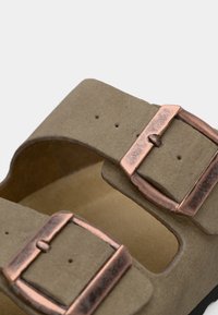 Sandale en suede gris avec deux boucles en ton cuivre, design ouvert, semelle intérieure rembourrée et dessus texturé. Positionnée pour une vue de côté.