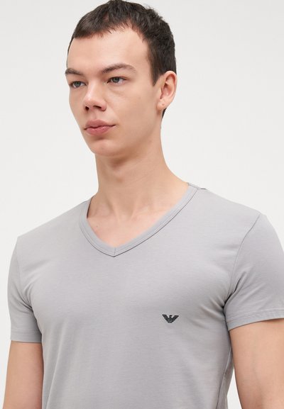 Helles graues, kurzärmliges Baumwoll-T-Shirt mit V-Ausschnitt und kleinem schwarzen Logo auf der linken Brust. Glatte Textur und klassischer Schnitt.