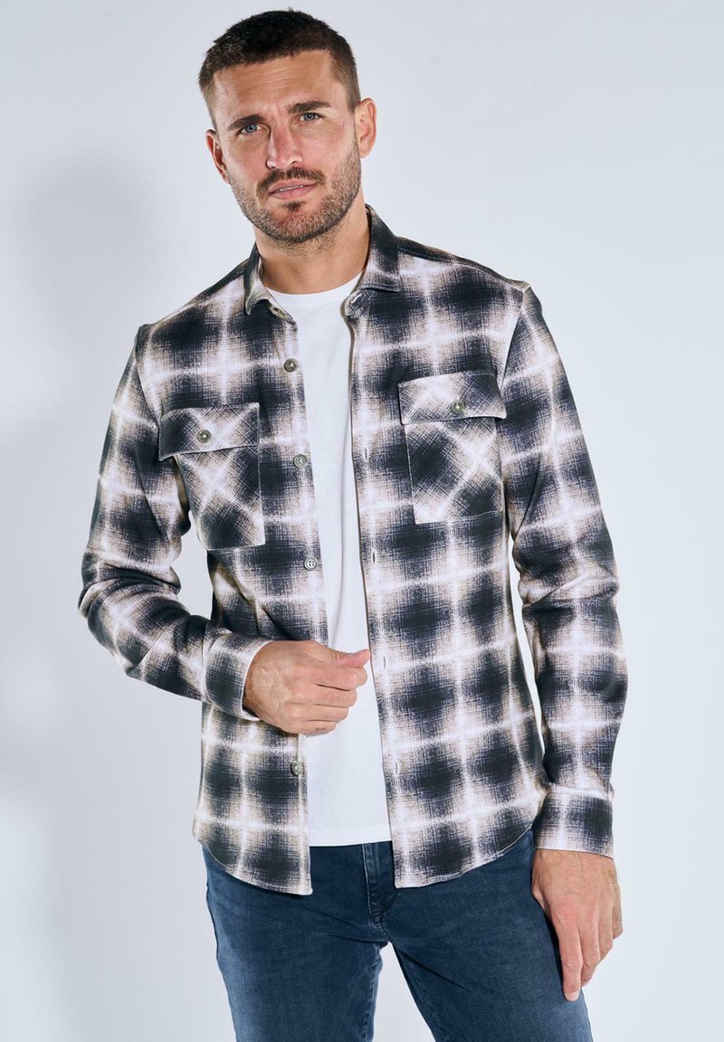 Schwarz-weißer kariert flanellhemden mit Knopfleiste, zwei Brusttaschen und langen Ärmeln. Getragen über einem weißen T-Shirt.