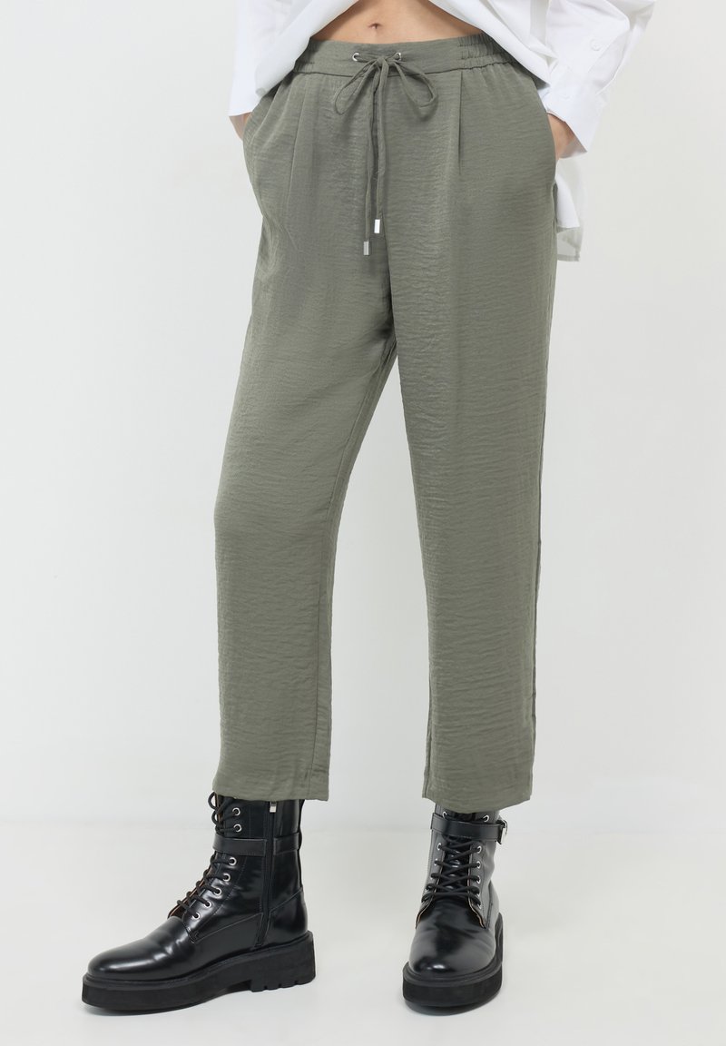 Pantalons légers olive avec une finition texturée, dotés d'une taille élastique avec cordon de serrage et de poches latérales, associés à des bottes de combat noires.