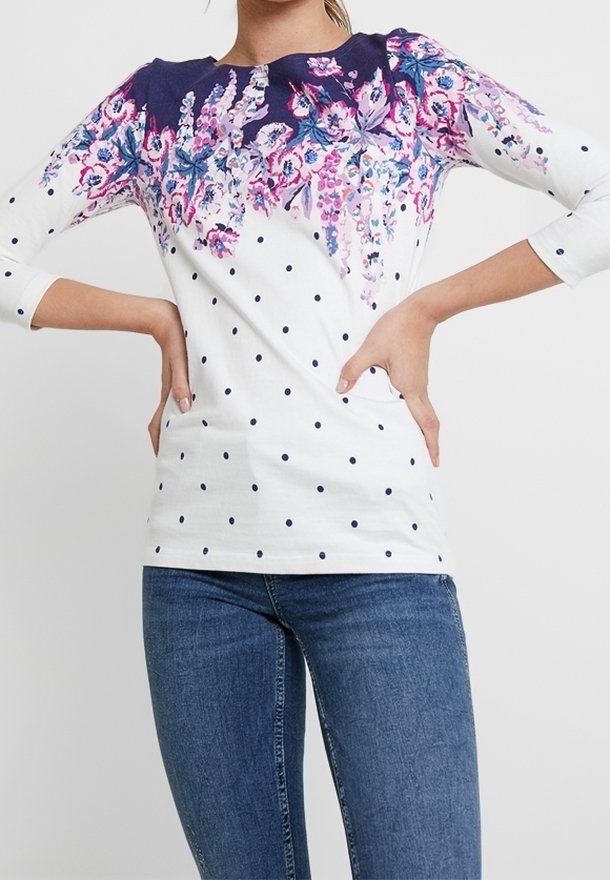 Witte langekleurige top met bloemenprint in tinten van roze en blauw op de schouders, met marineblauwe stippen op de onderzijde.
