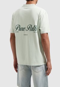 Lichtgroene katoenen T-shirt met korte mouwen, voorzien van de tekst "Pure Path" in donkergroen op de achterkant en een ontspannen pasvorm.