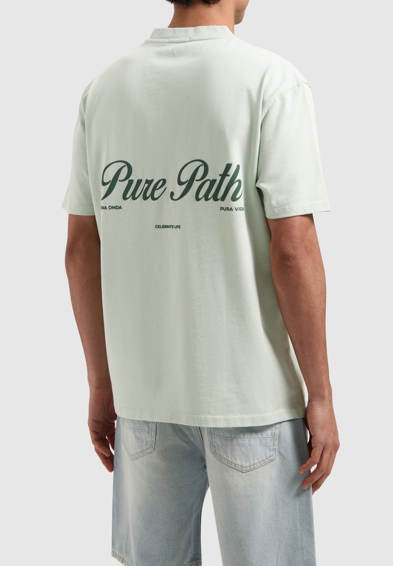 Lichtgroene katoenen T-shirt met korte mouwen, voorzien van de tekst "Pure Path" in donkergroen op de achterkant en een ontspannen pasvorm.