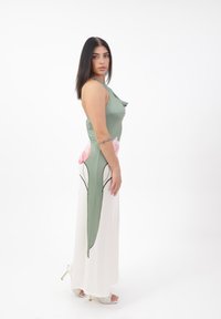 Langes Kleid mit einem grünen, enganliegenden Oberteil und einem fließenden weißen Rock, der rosa Blumenmuster trägt. Glatte Textur, ärmelloses Design und seitlicher Schlitz.