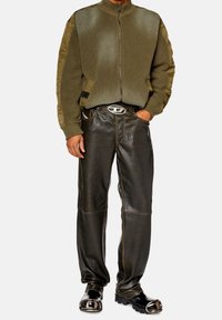 Olivgrön zip-up bomberjacka med texturerad framdel, i kombination med mörka läderbyxor med paneler och kontrastsömmar. Svarta skor med metalliska detaljer.