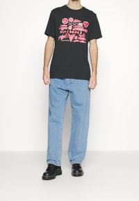Camiseta de algodón negra con diseños gráficos multicolores; combinada con jeans holgados de color azul claro y zapatos negros.