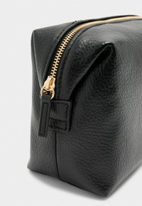 Borsa in pelle nera con finitura testurizzata, dotata di chiusura con zip dorata e lati inclinati per un design compatto.