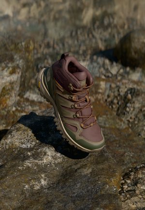 Buty do wędrówek z fioletowo-zielonym górnym materiałem kompozytowym, wzmocnionym noskiem, brązowymi sznurówkami, teksturowaną podeszwą i agresywnym wzorem bieżnika.