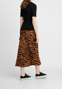 Černý top s krátkým rukávem spárovaný s oranžovou sukní do kolen, která má černý pruhovaný vzor tygra, doplněný černými botami.