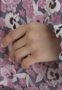 A human hand rests against a floral-patterned fabric, featuring shades of pink, purple, and white, with a smooth texture and relaxed posture.