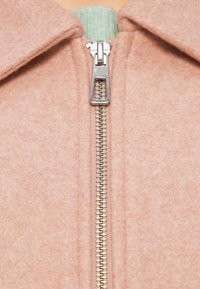 Ροζ ανοιχτή ζακέτα με ασημένιο φερμουάρ, με πράσινο ριμπ γιακά. Κατασκευασμένη από απαλό, υφή υφασμάτων.