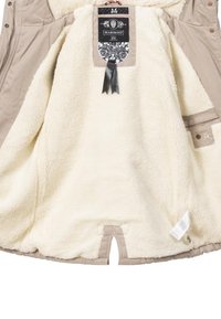 Beige outer jacket lined with cream, fluffy faux fur. Features a hanging label, front pockets, and a small cutout at the hem.