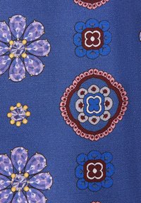 Tissu bleu avec divers motifs floraux stylisés en violet, rose, rouge, blanc, jaune et bleu, disposés selon une grille diagonale.