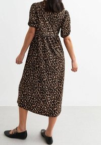 Šaty s leopardím potiskem, krátkými puff rukávy, ke kolenům a s nařaseným pasem. Kombinováno s černými balerínami se zdobnými pásky.