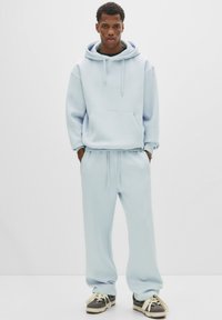 Lichtblauwe hoodiesweater met een voorzak, gecombineerd met bijpassende joggingbroek. Zacht materiaal, relaxte pasvorm en elastische boorden op de broek.