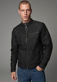 Chaqueta de cuero negro con un alto cuello, cremallera frontal y bolsillos con cremallera en los laterales; textura suave con detalles de costura mínimos.