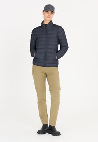 Marinblå puffjacka med quiltad textur, dragkedja framtill och sidofickor, ihopparad med khakifärgade cargobyxor och svarta robusta stövlar.