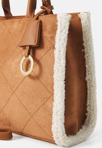 Burgundu zamšas iepirkumu soma ar quilted rakstu, krēmveida teksturētu apdari un zelta gredzena akcentu. Ir ādas rokturi un noņemams siksna.
