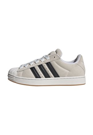 Jasnoszare sneakersy z zamszu z białymi sznurowadłami, czarnymi trzema paskami po bokach oraz białym gumowym noskiem i podeszwą.