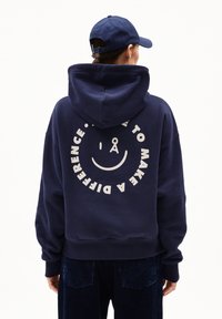 Felpa navy con un grande grafico bianco di un volto sorridente e la scritta "FAI LA DIFFERENZA" sul retro. Presenta un cappuccio spazioso e spalle abbassate.