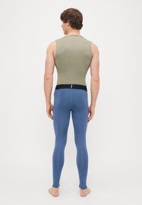 Αθλητικά ρούχα που περιλαμβάνουν ένα προσαρμοσμένο, αμάνικο ελαιόχρωμο τοπ και μπλε κολάν. Το τοπ έχει μια μαύρη λωρίδα με λογότυπο στον λαιμό.