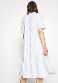 Abito in cotone bianco con un design a strati, maniche corte e gonna fluida. Il tessuto ha una texture liscia con una vestibilità comoda.