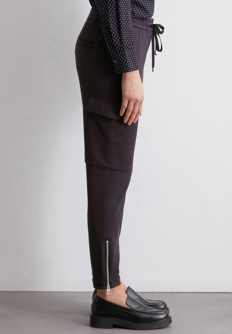 Czarne dresowe spodnie z boczną kieszenią cargo, regulowanym paskiem w talii, zamkami na kostkach oraz dopasowanym krojem. Gładka faktura z minimalnymi detalami.