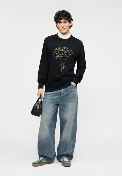 Μαύρο φούτερ με χρυστό λουλουδένιο σχέδιο, συνδυασμένο με άνετο ανοιχτό μπλε τζιν και πράσινα αθλητικά παπούτσια. Αξεσουάρ: μικρή μαύρη τσάντα.