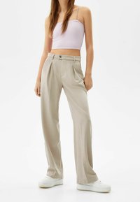 Licht beige geplooide broek met een rechte pasvorm, gecombineerd met een lavendel geribde crop top en witte sneakers.