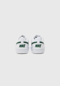 Baskets blanches avec des accents verts, dotées d'une semelle en caoutchouc, d'un collier rembourré et d'un logo sur le talon. Matériau lisse imitant le cuir et design minimaliste.