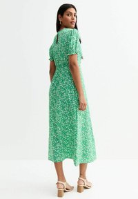 Vestido midi floral verde con mangas cortas tipo globo, detalle de keyhole en la espalda y un corte relajado. Estilizado con sandalias de tacón bloque en color beige.