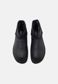 Botas negras hasta el tobillo con un acabado de ante suave, punta redondeada, costura texturizada y forro de piel suave en el cuello.