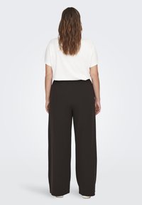 Pantalones negros de pierna ancha con una textura suave y cinturilla elástica, combinados con una camiseta blanca de corte holgado, mostrados desde la parte posterior.