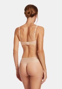 Nude bralette en bijpassende slip, naadloos ontwerp, verstelbare banden, gladde textuur, minimale hardware, moderne snit met een lage taille.