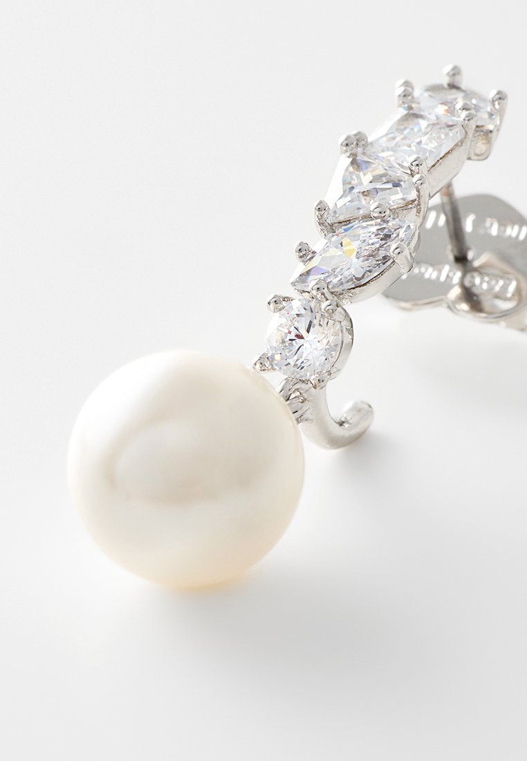 Ein einzelner silberner Ohrring mit einer großen runden Perle und einer geschwungenen Reihe von fünf klaren, funkelnden Edelsteinen.