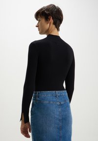 Top a coste nero con un design aderente e maniche lunghe, abbinato a una gonna in denim azzurro chiaro con un taglio di media lunghezza e fessure laterali.