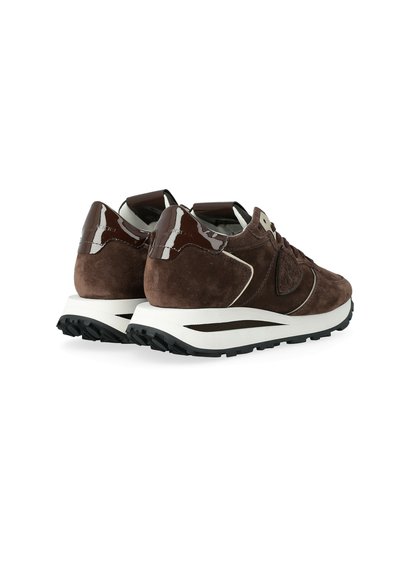 Un paio di sneaker in suede marrone con suole intermedie bianche, suole nere e tappi del tallone lucidi di un marrone scuro, mostrati da un'angolazione posteriore.