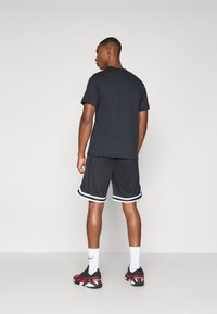 Camiseta de algodón negra con mangas cortas, combinada con pantalones cortos deportivos negros con rayas blancas. El calzado incluye zapatillas rojas y negras.