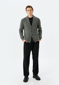 Grauer, gestrickter Cardigan mit einem Schalkragen und drei Knöpfen, kombiniert mit einem schwarzen Shirt und lockeren schwarzen Hosen. Glatte Textur und lässige Passform.